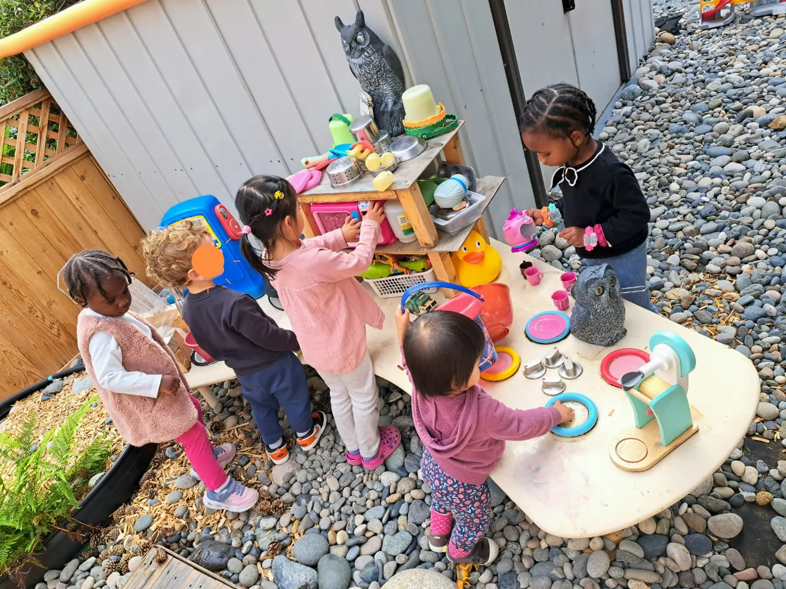 Children exploring an outdoor water table and pretend-play toys
