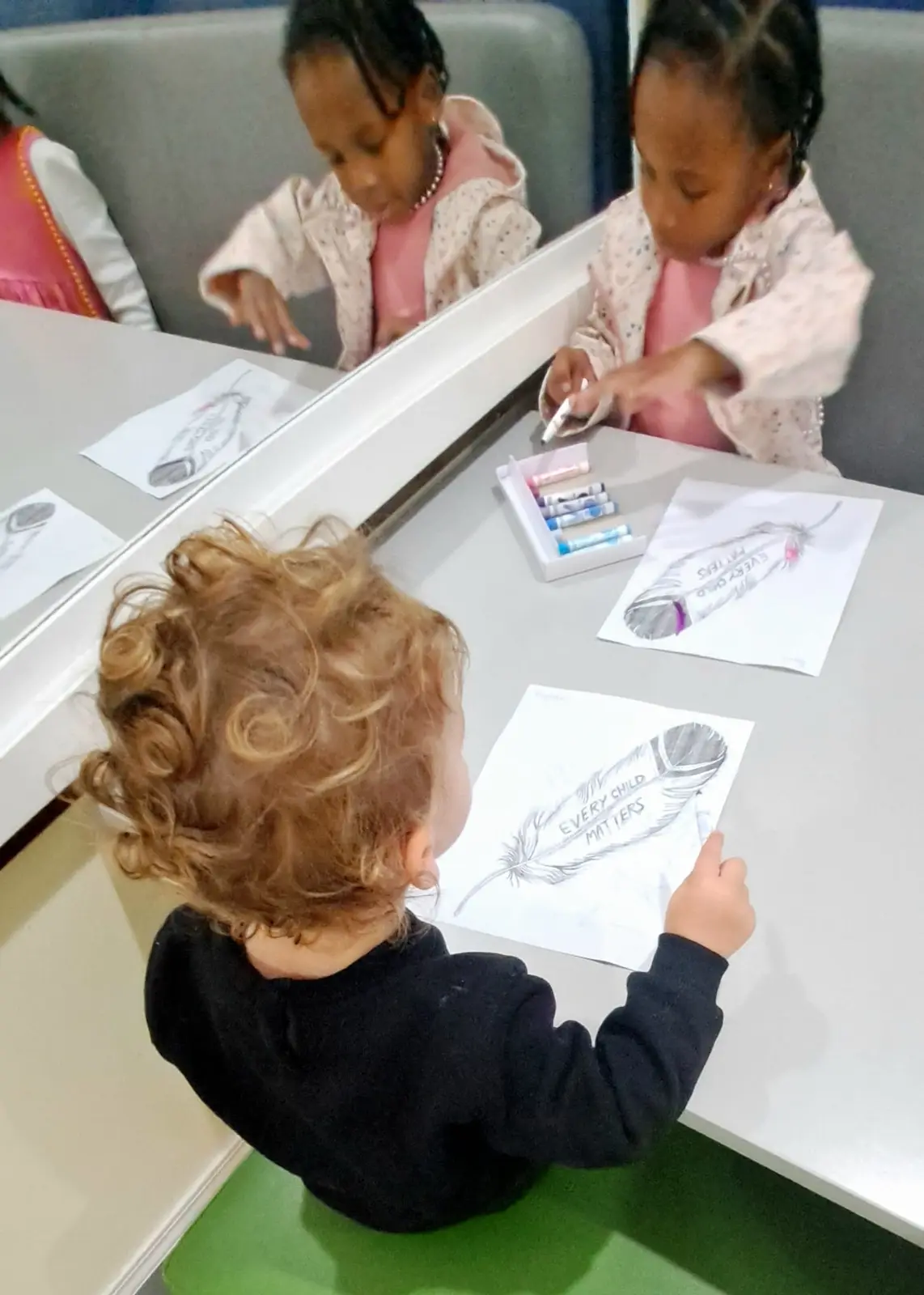Children coloring feather artwork at a table